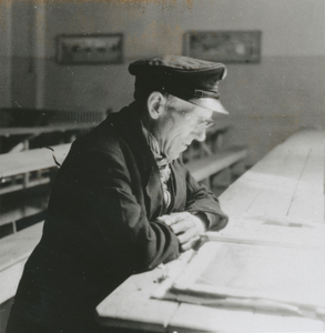876767 Afbeelding van vermoedelijk een evacuee die de krant leest in een klaslokaal van de Piusschool (Oudegracht 33) ...